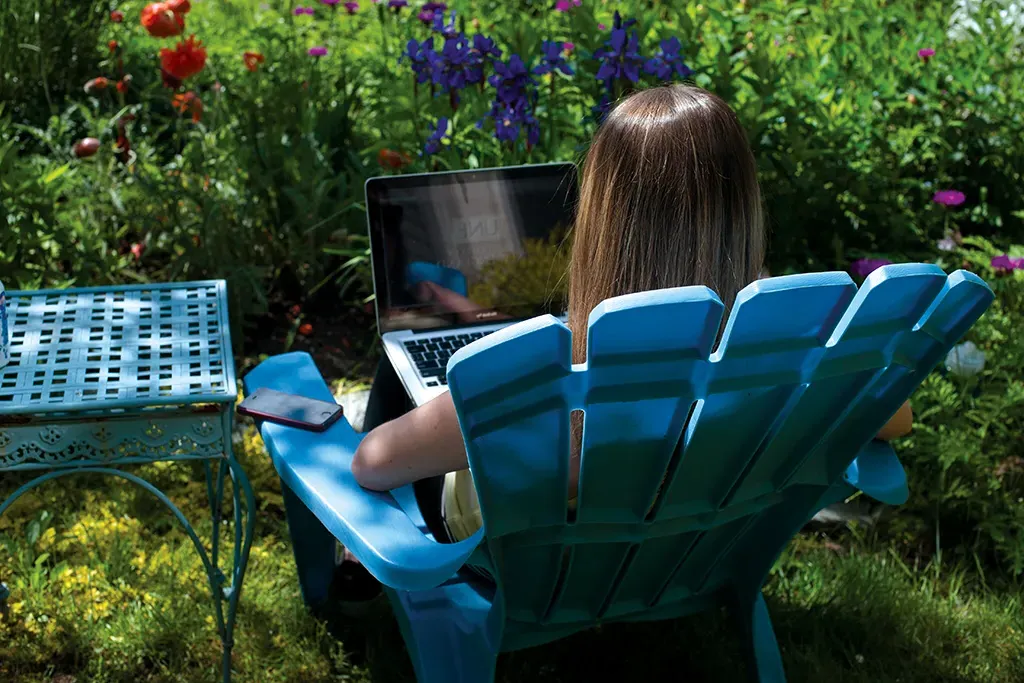 A U N E student types on a laptop while sitting outside