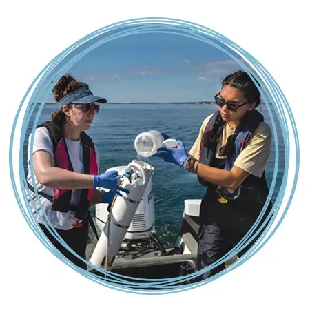 Two marine science students filling a sampling container with ocean water