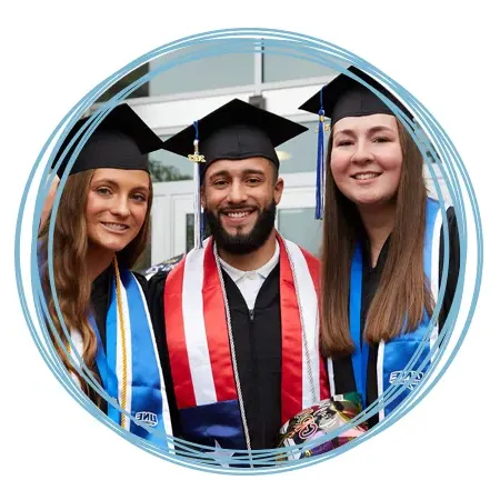 Three students stand together in their academic regalia before their graduation ceremony