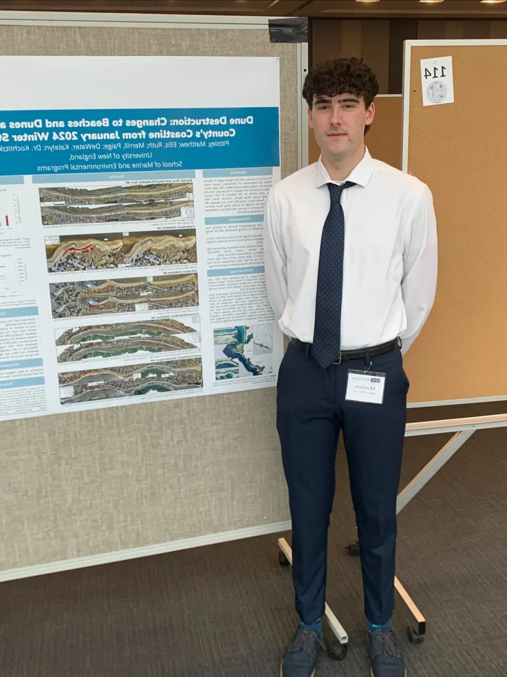 A UNE student (Matthew Pittsley) poses in front of a research poster