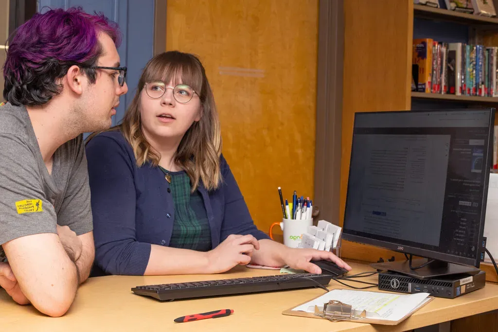 A student looks up research articles on a computer with the U N E librarian