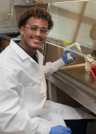 A student researcher smiles while holding lab equipment