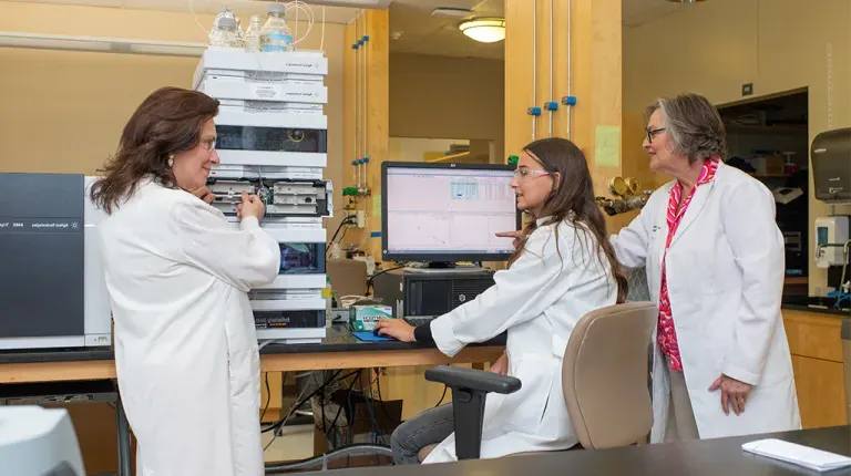 Karen Houseknecht points at a coputer screen while a UNE student in a chair looks over to another researcher 