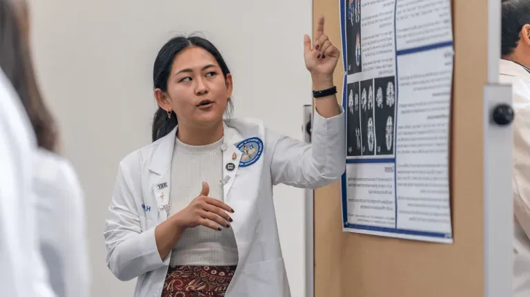 A medical student presents a research poster to a group of people