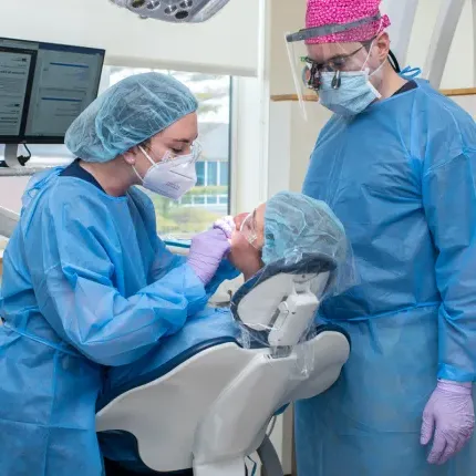 A dental student and a physician assistant student look into the mouth of a patient during a dental screening