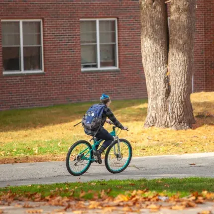 A student riding a bike on a paved path on the Biddeford Campus