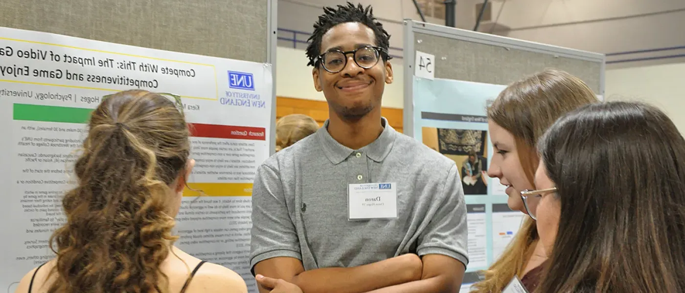 A student speaks about their poster presentation to three people