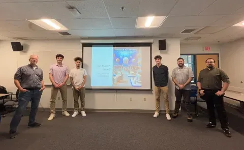 UNE students pose in front of a slideshow presentation with members of the DeepWater Buoyancy sales team